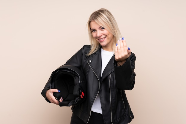 Foto joven rubia con un casco de moto sobre pared aislada invitando a venir con la mano. feliz de que hayas venido