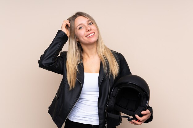 Joven rubia con un casco de moto sobre pared aislada riendo