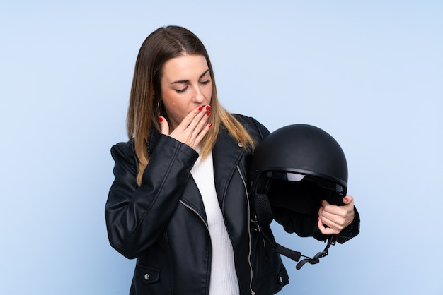 Joven rubia con un casco de moto sobre pared aislada con sorpresa y expresión facial conmocionada