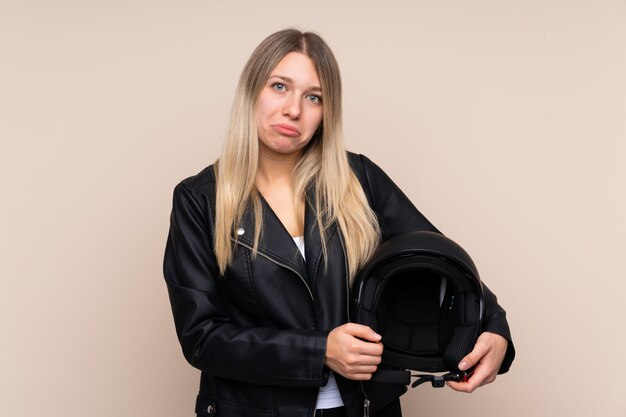 Joven rubia con un casco de moto sobre pared aislada suplicando