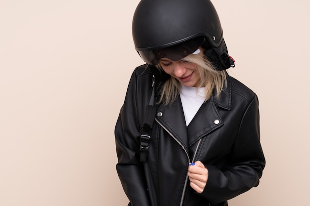 Joven rubia con un casco de moto sobre pared aislada