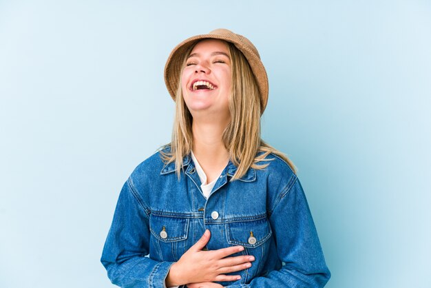 Joven rubia caucásica aislada se ríe alegremente y se divierte manteniendo las manos en el estómago.