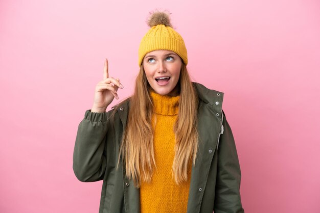 Joven rubia con chaqueta de invierno aislada de fondo rosa con la intención de darse cuenta de la solución mientras levanta un dedo