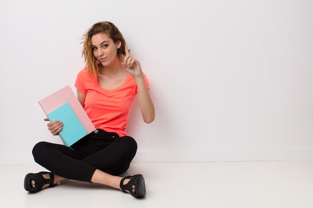 Joven rubia contra la pared de color plano con libros