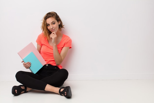 Joven rubia contra la pared con libros