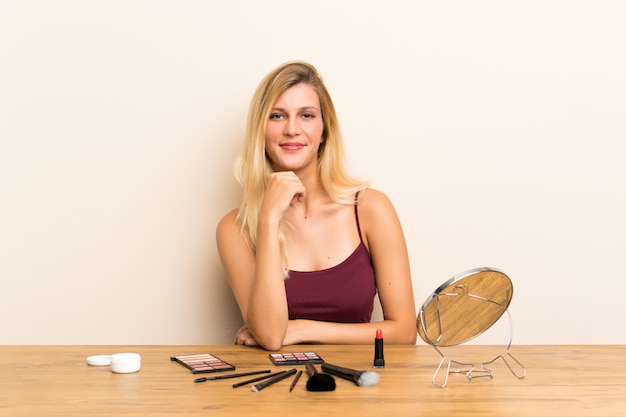 Joven rubia con cosmética en una mesa riendo