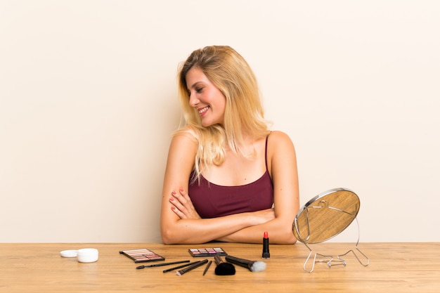 Joven rubia con cosmética en una mesa riendo