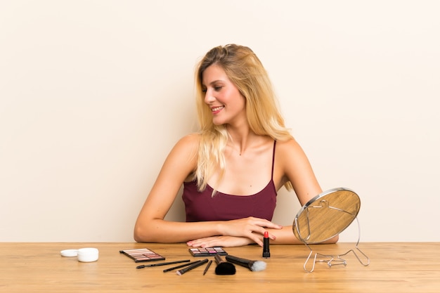 Joven rubia con cosméticos en una mesa mirando hacia el lado