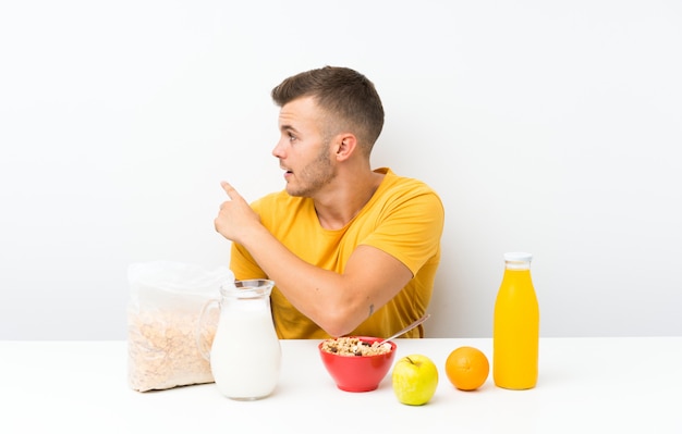 Joven rubia desayunando apuntando hacia atrás con el dedo índice