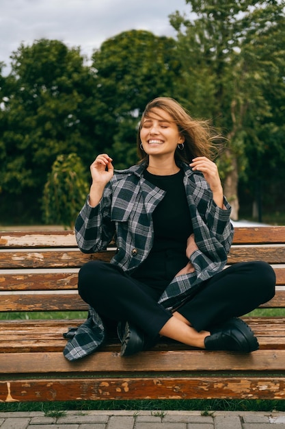 La joven rubia se divierte cuando hace viento mientras se sienta en un banco