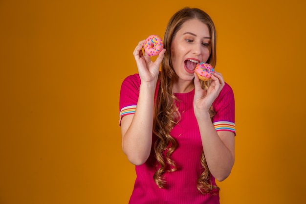 Foto joven rubia con donas sobre fondo amarillo.