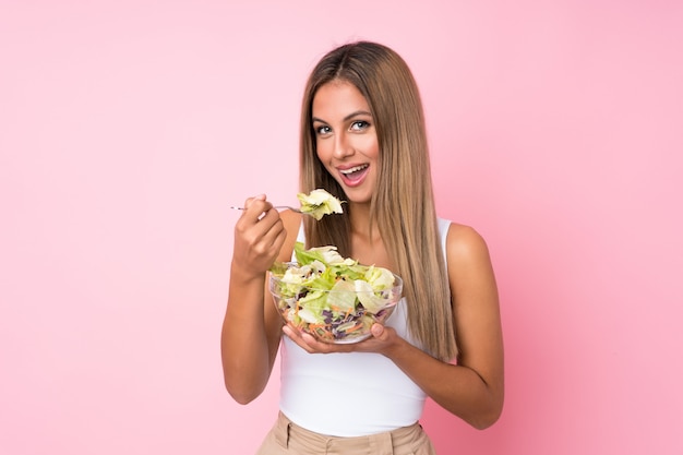 Joven rubia con ensalada sobre pared aislada