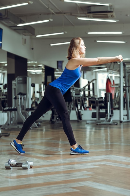 Joven rubia esbelta haciendo ejercicios en el gimnasio