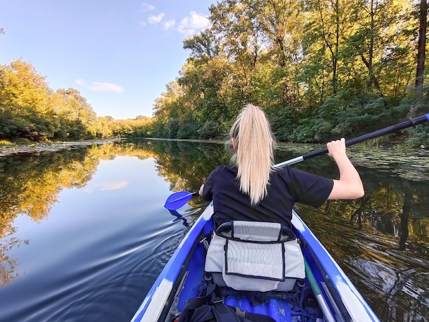 Una joven rubia está remando en un kayak vista trasera Turismo y recreación al aire libre