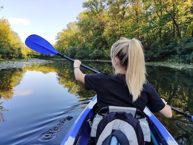 Una joven rubia está remando en un kayak vista trasera Turismo y recreación al aire libre