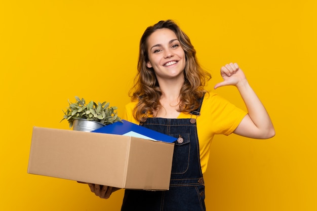 Joven rubia haciendo un movimiento mientras levanta una caja llena de cosas orgullosas y satisfechas