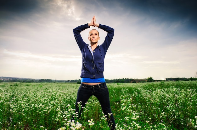 Joven rubia haciendo yoga en un prado