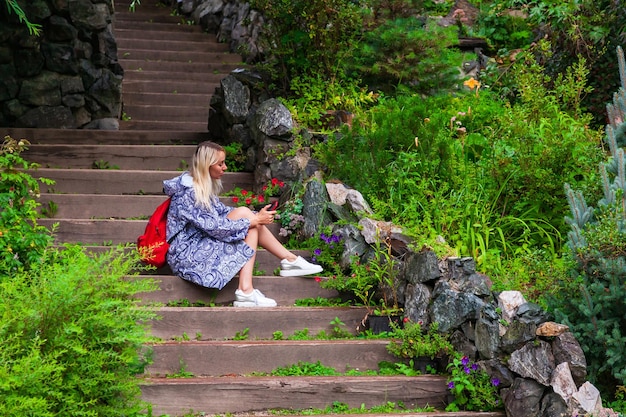 Una joven rubia hermosa con un impermeable azul se sienta en una escalera de madera con paredes de piedra