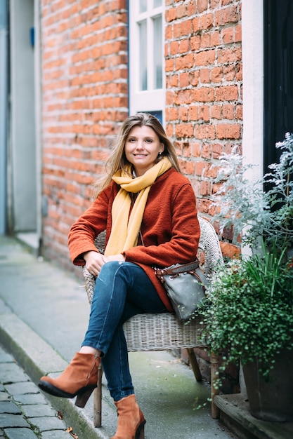 Una joven rubia hermosa está sentada en una silla y disfrutando de una pequeña calle urbana en lubeck.