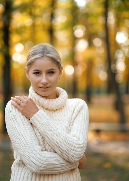 Una joven rubia hermosa con un suéter blanco camina en el parque de otoño