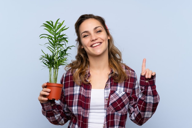 Joven rubia jardinero chica sosteniendo una planta apuntando hacia una gran idea