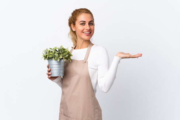 Joven rubia jardinero mujer niña sosteniendo una planta sobre pared blanca con espacio en blanco imaginario en la palma