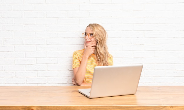 joven rubia en laptop sintiendo pensativo preguntándose