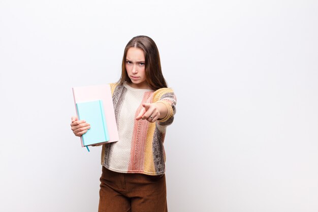 Joven rubia con libros contra la pared blanca