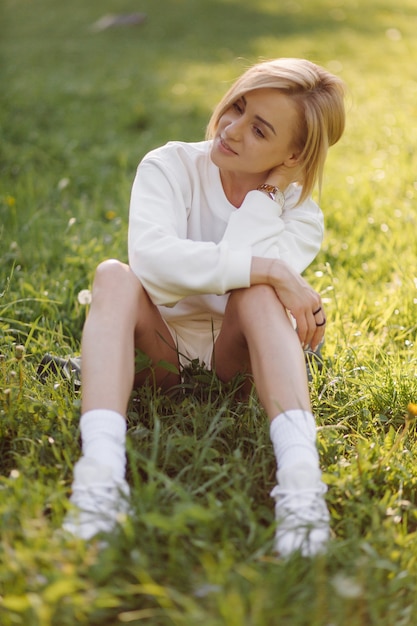 Joven rubia lleva una sudadera con capucha blanca sonriendo y caminando en el bosque