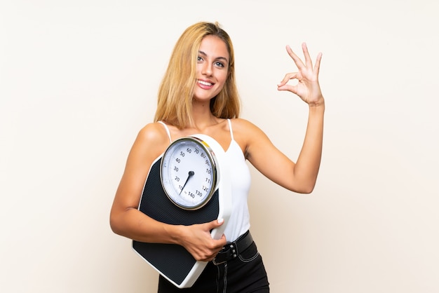 Joven rubia con máquina de pesaje haciendo signo de OK