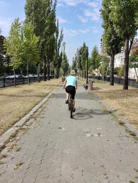 Una joven rubia monta una bicicleta a lo largo del callejón en perspectiva vista trasera Turismo y deportes