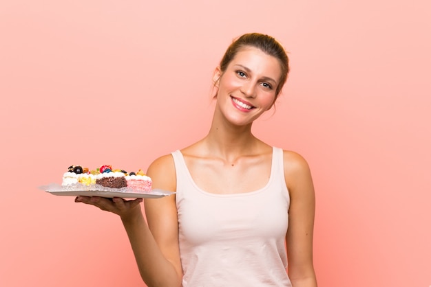 Joven rubia con un montón de diferentes mini pasteles sonriendo mucho