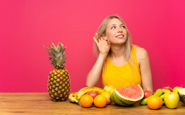 Joven rubia con muchas frutas escuchando algo