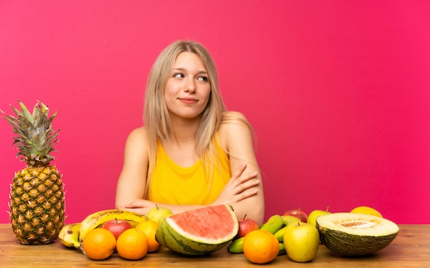 Joven rubia con muchas frutas pensando en una idea.