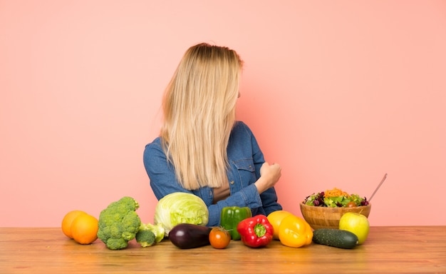 Joven rubia con muchas verduras apuntando hacia atrás