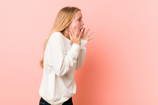 Joven rubia mujer adolescente grita fuerte, mantiene los ojos abiertos y las manos tensas.