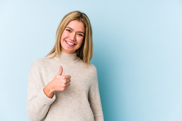 Joven rubia mujer caucásica aislada sonriendo y levantando el pulgar hacia arriba