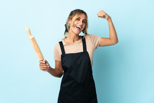 Joven rubia mujer cocina uruguaya aislada sobre pared azul haciendo gesto fuerte