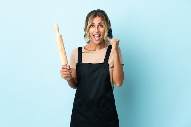 Joven rubia mujer cocina uruguaya en azul celebrando una victoria en la posición ganadora