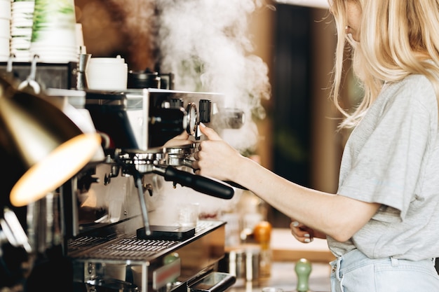 Una joven rubia muy delgada, vestida con ropa informal, está cocinando café en una cafetería popular. .