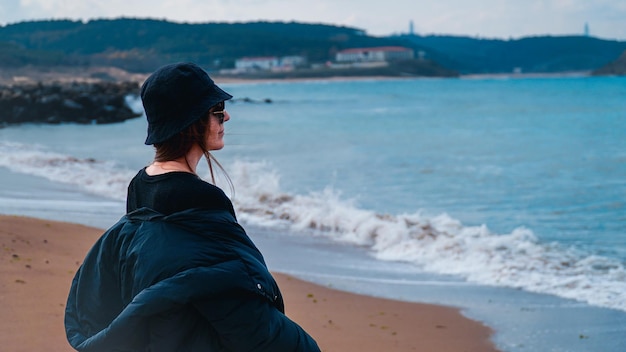 Foto joven rubia parada sola junto al mar mirando el horizonte y pensando.