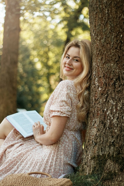 Joven rubia en el parque de verano lee el libro