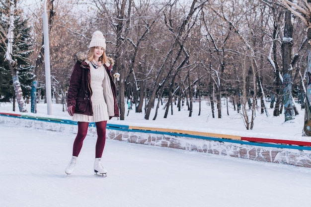Joven rubia patinando en el parque de invierno cubierto de nieve.