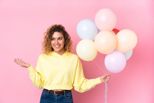 Joven rubia con el pelo rizado atrapar muchos globos en rosa riendo