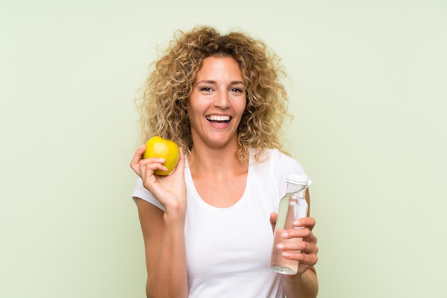 Joven rubia con el pelo rizado con una manzana y con una botella de agua