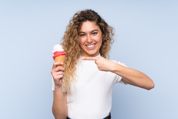 Joven rubia con el pelo rizado sosteniendo un helado de corneta en azul y apuntando