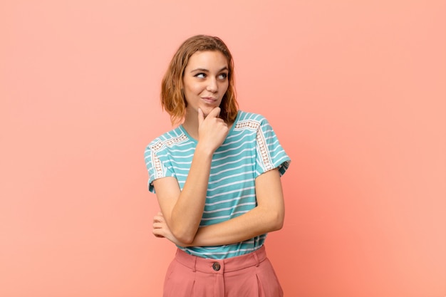 Joven rubia pensando, sintiéndose dudosa y confundida, con diferentes opciones, preguntándose qué decisión tomar sobre la pared de color