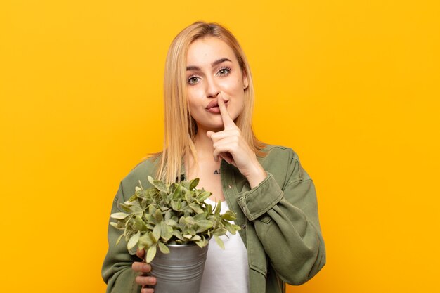 Joven rubia pidiendo silencio y silencio, gesticulando con el dedo delante de la boca, diciendo shh o guardando un secreto