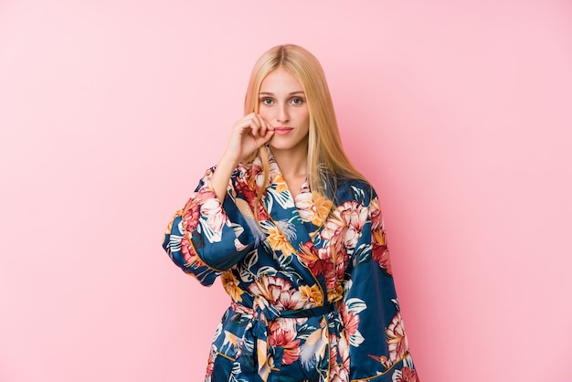 Joven rubia con un pijama de kimono con los dedos en los labios guardando un secreto.