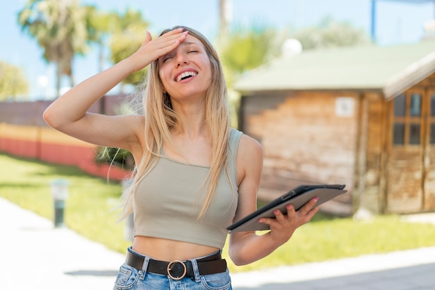 Una joven rubia que sostiene una tableta al aire libre se ha dado cuenta de algo y tiene la intención de encontrar la solución